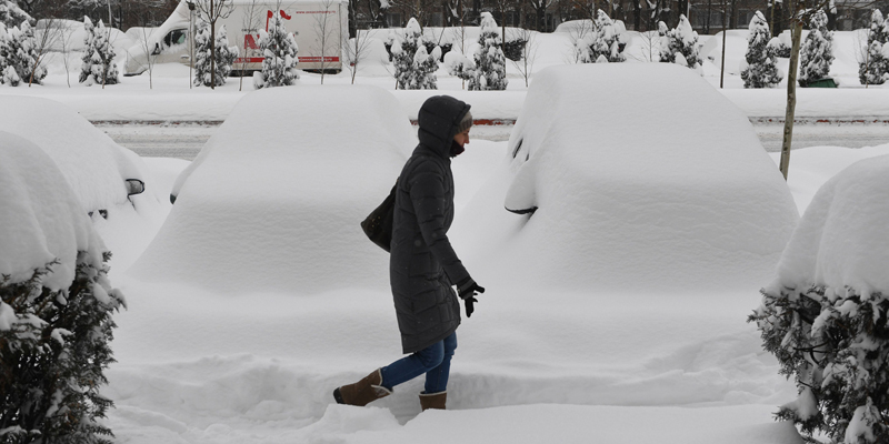 A woman walks in the snow next to snow covered automobiles in Bucharest on January 11, 2016. Southeasthern Romania was hit again by a snow storm causing havoc on the railway and road transportation. The cold spell in Europe has caused six deaths in Romania since Thursday, according to a first official report drawn up Tuesday by the Ministry of Health for AFP. / AFP PHOTO / DANIEL MIHAILESCU