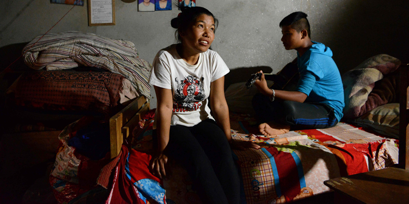 In this photograph taken on April 11, 2017, Nepalese earthquake survivor Sarita Tamang (L) looks on as her son plays a guitar in their home in Chutara, some 100kms east of Kathmandu. With just seven health workers for every 10,000 people, Nepal was grossly ill-equipped when the massive 7.8-magnitude earthquake struck on April 25, 2015, levelling whole villages and killing 9,000.  / AFP PHOTO / Prakash MATHEMA / To go with 'Nepal-quake-anniversary-disability' FEATURE by Annabel SYMINGTON