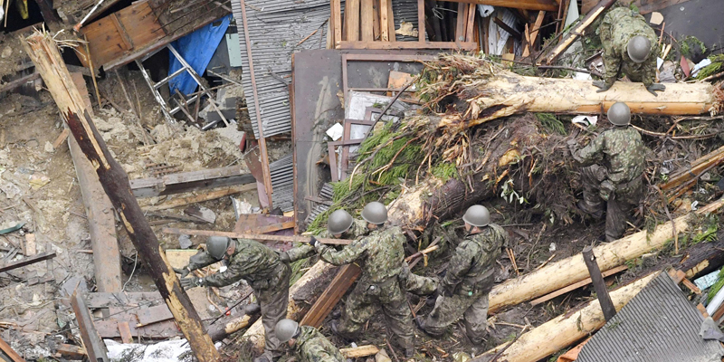 Rescue workers from Japan's Self Defense Force search through debris piled over a house completely demolished by flooding caused by heavy rain in Toho, Fukuoka prefecture, southwestern Japan Thursday, July 6, 2017. Troops worked Thursday to rescue hundreds of people stranded by flooding in southern Japan. (Nozomu Endo/Kyodo News via AP)