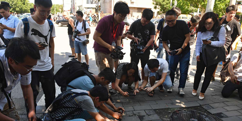 Journalists take photos of scattered glass and blood on the pavement outside the US embassy compound in Beijing on July 26, 2018 following a blast near the embassy premises. A 26-year-old Chinese man set off a small explosive device outside the US embassy in Beijing on July 26, injuring his hand in the blast before he was taken into custody, police said. / AFP PHOTO / Greg BAKER