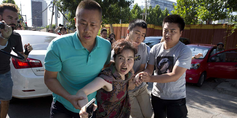 A woman is dragged away by Chinese men moments after she was seen talking to journalists near the site of a reported explosion outside the U.S. Embassy in Beijing, China, Thursday, July 26, 2018. A man exploded a small homemade bomb outside the U.S. Embassy in Beijing on Thursday, injuring only himself, according to police and an embassy spokesperson. (AP Photo/Ng Han Guan)