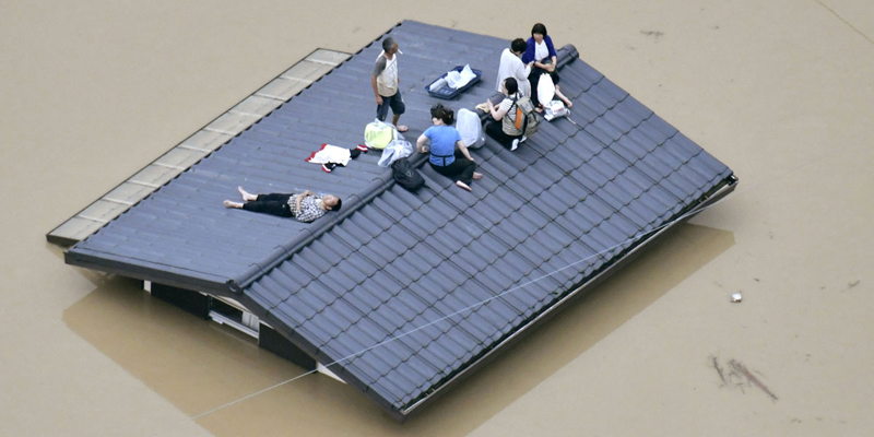 People waif to be rescued on the top of a house almost submerged in floodwaters caused by heavy rains in Kurashiki, Okayama prefecture, southwestern Japan, Saturday, July 7, 2018. 